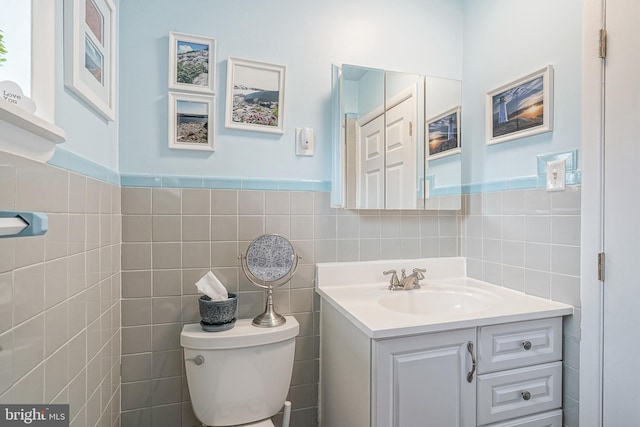 half bathroom featuring wainscoting, vanity, toilet, and tile walls