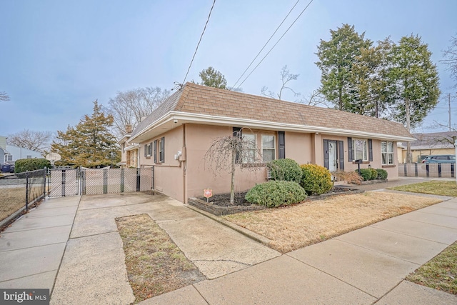 view of front of home featuring a shingled roof, fence, mansard roof, and stucco siding