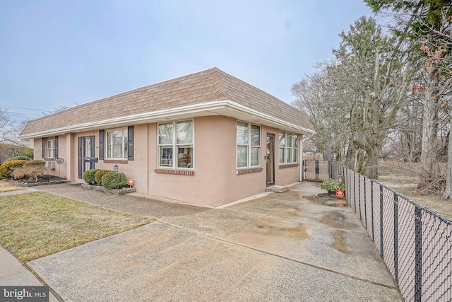 view of home's exterior featuring a shingled roof, mansard roof, fence, and stucco siding