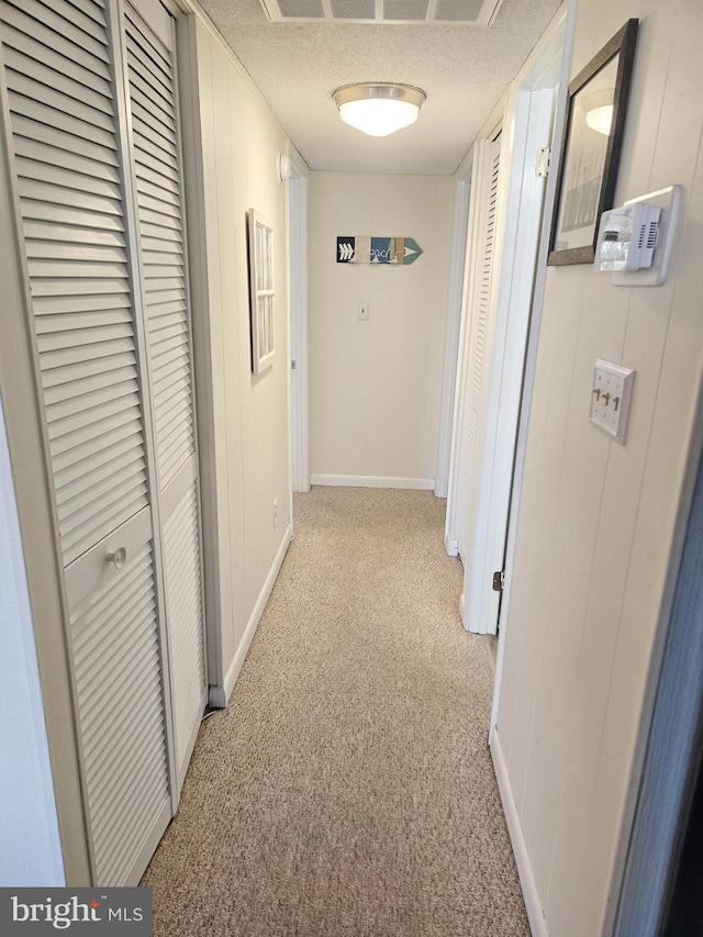 hallway with light colored carpet and a textured ceiling