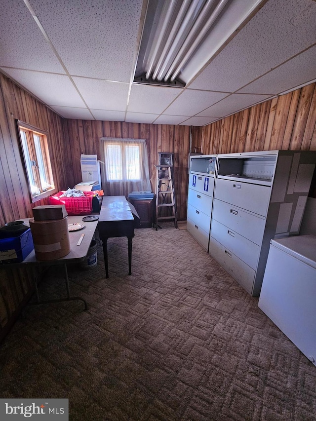 unfurnished office with carpet floors, a paneled ceiling, and wood walls