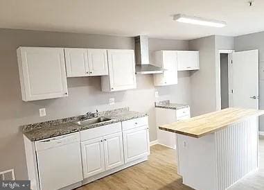 kitchen with dishwasher, sink, white cabinets, a center island, and wall chimney exhaust hood