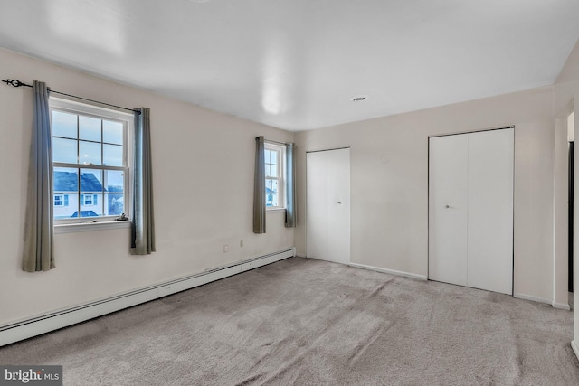 unfurnished bedroom featuring baseboard heating, light colored carpet, and multiple closets