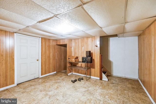 basement featuring a paneled ceiling and wood walls