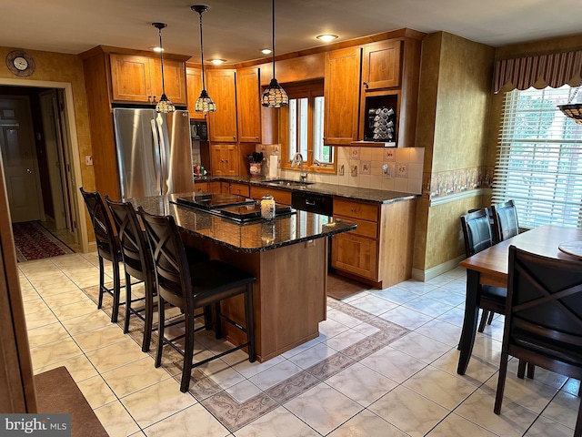 kitchen featuring stainless steel refrigerator, sink, a breakfast bar area, dark stone counters, and hanging light fixtures