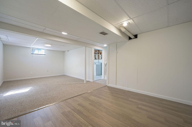 basement featuring wood-type flooring, washer / dryer, and a paneled ceiling