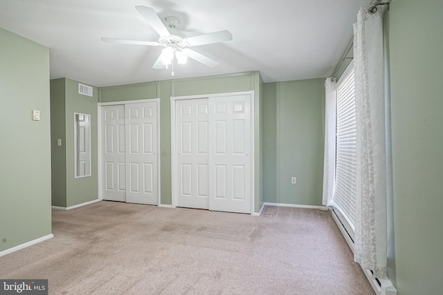 unfurnished bedroom with a baseboard radiator, two closets, light colored carpet, and ceiling fan