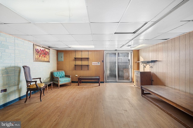 sitting room featuring wooden walls, a paneled ceiling, electric panel, and light wood-type flooring