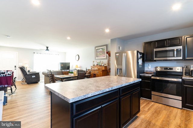 kitchen with stainless steel appliances, ceiling fan, a center island, and light hardwood / wood-style floors