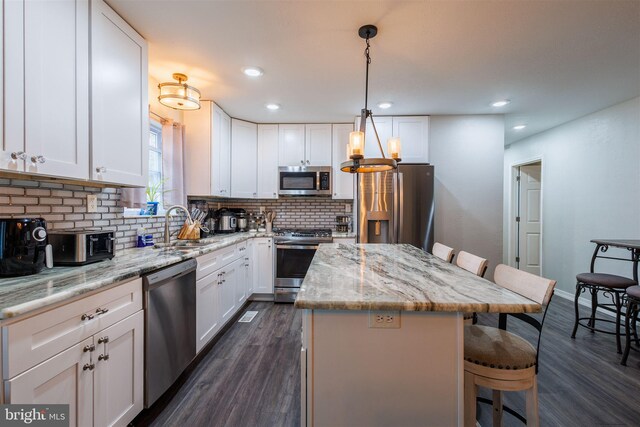 kitchen featuring stainless steel appliances, a kitchen island, white cabinets, and decorative light fixtures