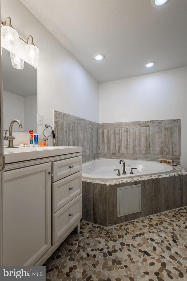 bathroom featuring a relaxing tiled tub and vanity