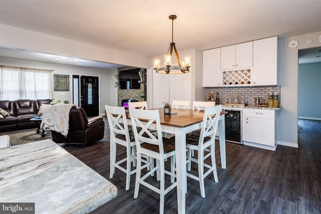 dining area with a stone fireplace, beverage cooler, dark hardwood / wood-style flooring, bar, and an inviting chandelier