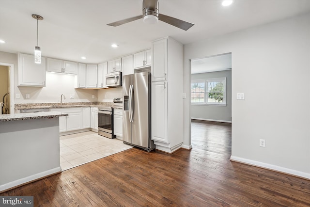 kitchen featuring decorative light fixtures, light stone countertops, appliances with stainless steel finishes, white cabinets, and wood finished floors