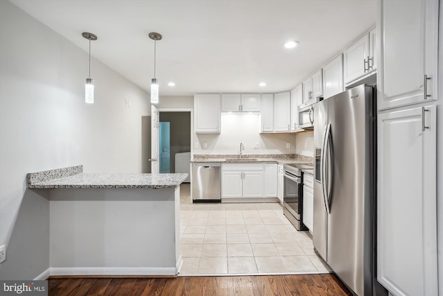 kitchen with a peninsula, light stone countertops, stainless steel appliances, white cabinetry, and a sink