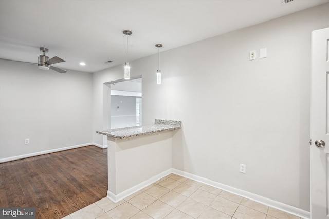 kitchen featuring light stone counters, decorative light fixtures, visible vents, a peninsula, and baseboards