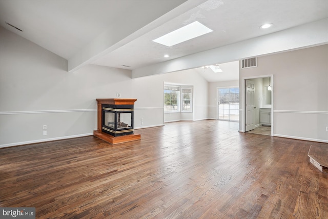 unfurnished living room featuring visible vents, a multi sided fireplace, wood finished floors, vaulted ceiling with skylight, and baseboards