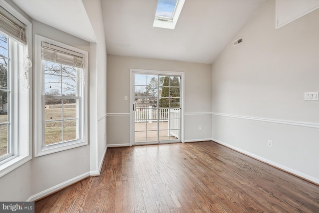 spare room featuring lofted ceiling with skylight, baseboards, visible vents, and wood finished floors