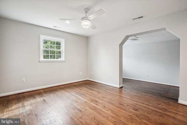 spare room featuring arched walkways, visible vents, baseboards, and wood finished floors