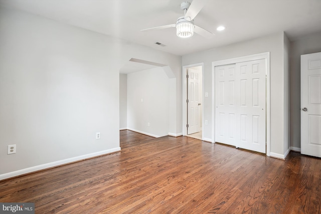 unfurnished bedroom featuring arched walkways, wood finished floors, and baseboards