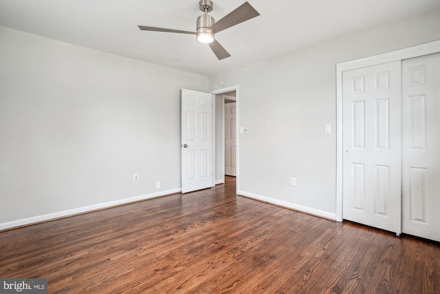 unfurnished bedroom with dark wood-type flooring, a closet, a ceiling fan, and baseboards