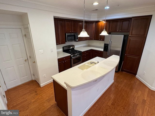 kitchen featuring appliances with stainless steel finishes, pendant lighting, an island with sink, wood-type flooring, and sink