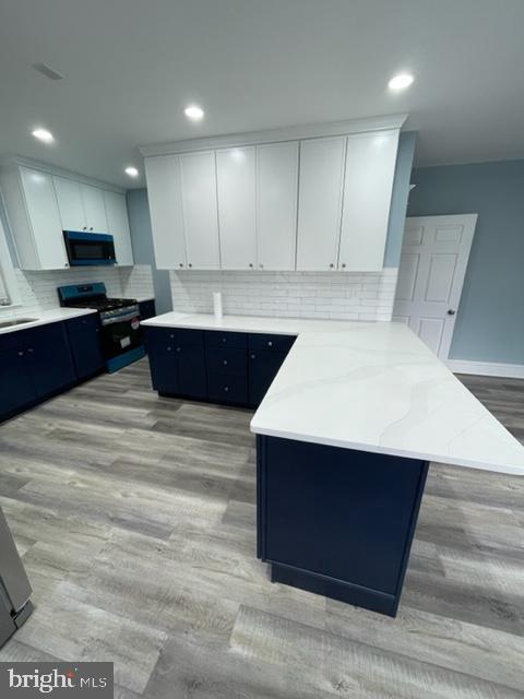 kitchen featuring a kitchen island, light stone counters, light hardwood / wood-style floors, white cabinets, and stainless steel range oven