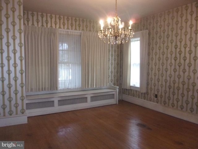 empty room featuring wood-type flooring, a chandelier, and radiator heating unit