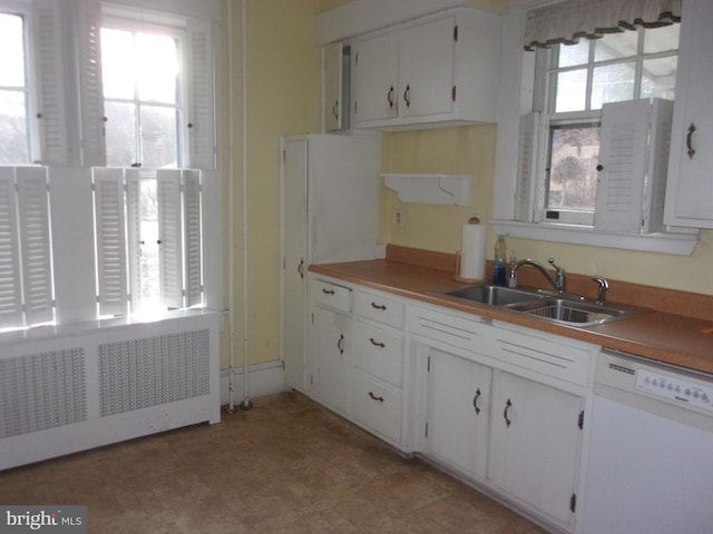 kitchen with white dishwasher, sink, white cabinetry, and radiator heating unit