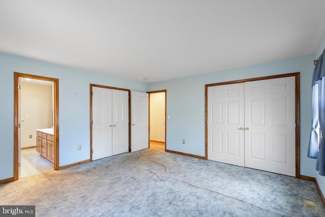 unfurnished bedroom featuring connected bathroom, light colored carpet, and two closets