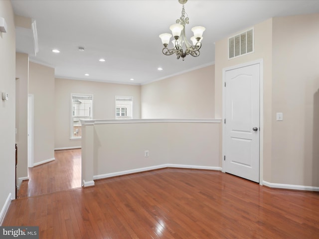 unfurnished room featuring an inviting chandelier, wood-type flooring, and ornamental molding