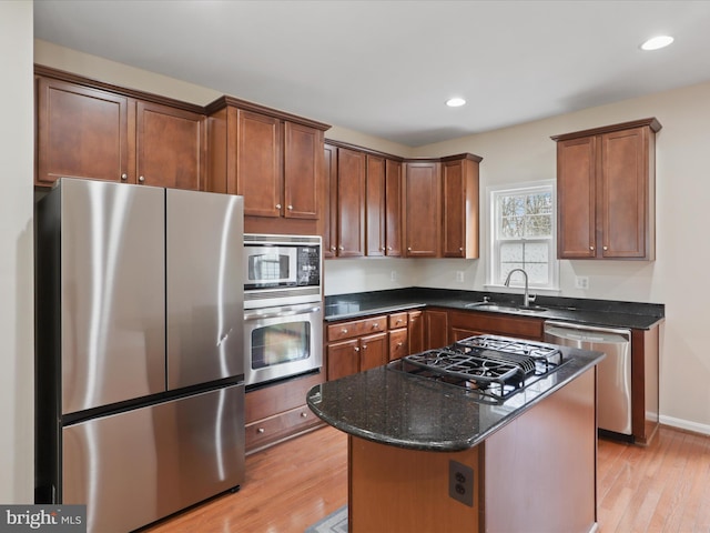 kitchen with sink, light hardwood / wood-style flooring, stainless steel appliances, a kitchen island, and dark stone counters