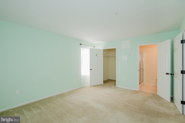 unfurnished bedroom with carpet floors, a closet, a spacious closet, and baseboards