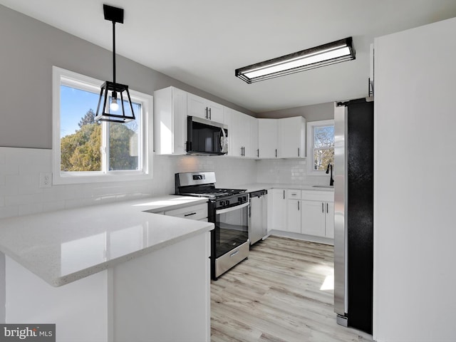 kitchen with stainless steel appliances, decorative light fixtures, white cabinets, and kitchen peninsula