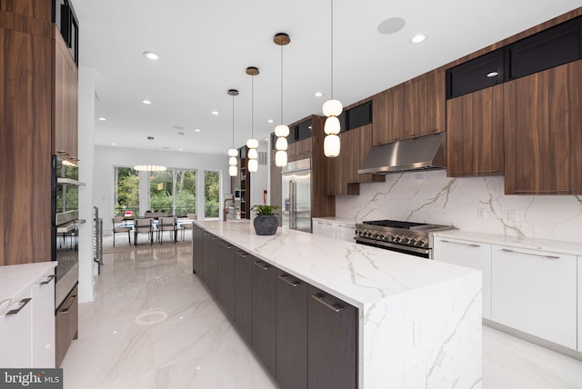 kitchen featuring hanging light fixtures, high quality appliances, light stone countertops, a kitchen island with sink, and white cabinets