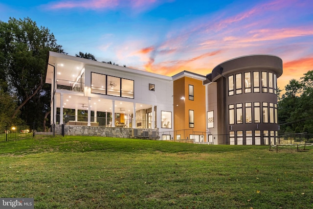 back house at dusk featuring a balcony and a lawn