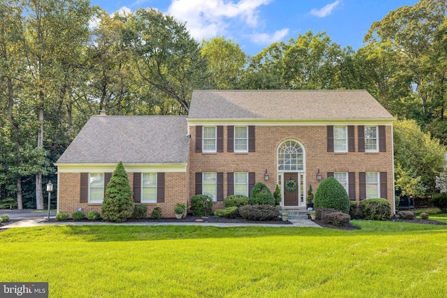 colonial inspired home featuring brick siding, roof with shingles, and a front yard