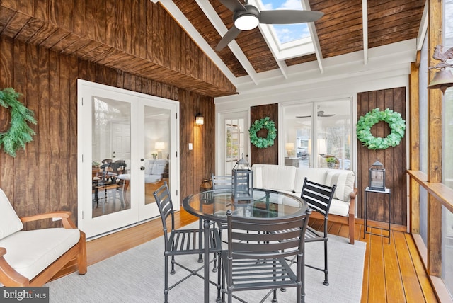 dining space with light wood finished floors, vaulted ceiling with skylight, ceiling fan, french doors, and wood walls