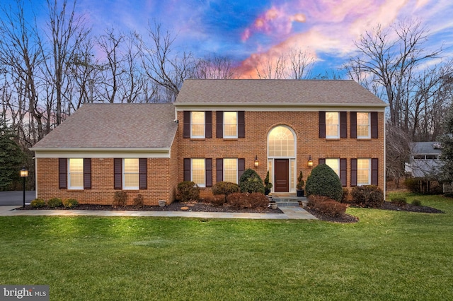 colonial-style house featuring a shingled roof, a front lawn, and brick siding