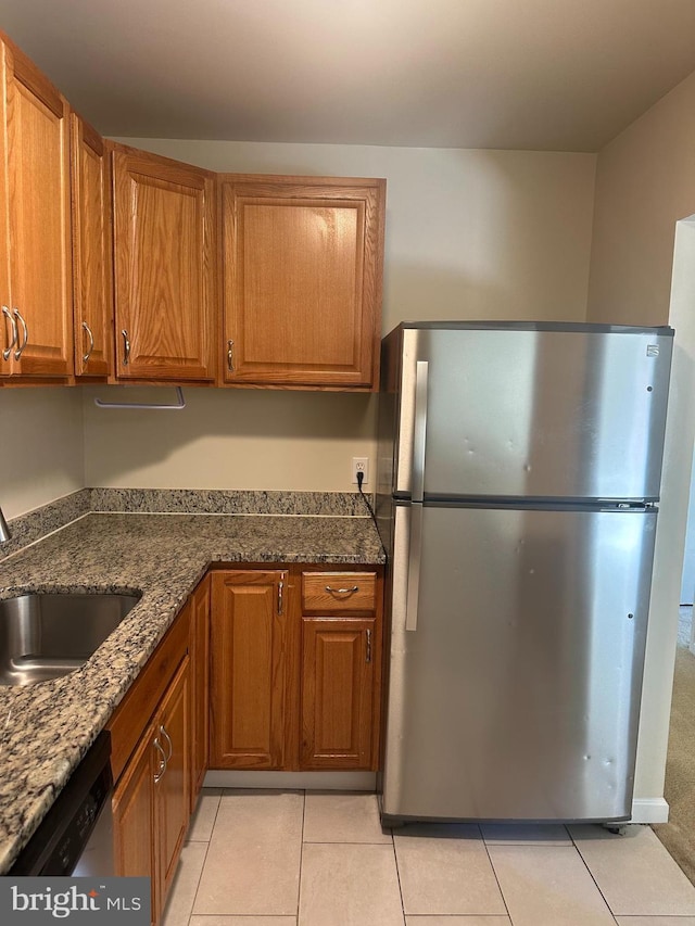 kitchen featuring stainless steel appliances, sink, light tile patterned floors, and dark stone counters