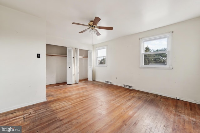 unfurnished bedroom featuring ceiling fan, light wood-type flooring, and two closets