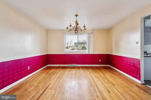 empty room with wood-type flooring and a chandelier