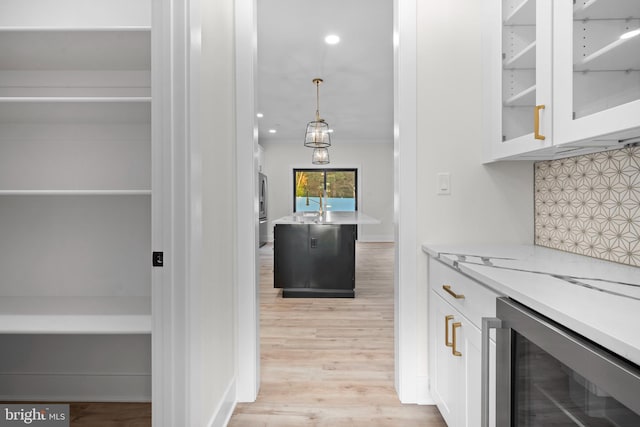 bar featuring wine cooler, light stone counters, decorative backsplash, white cabinets, and decorative light fixtures