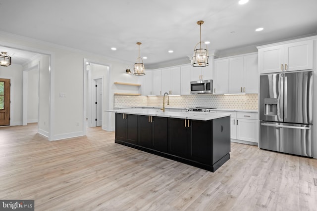 kitchen featuring tasteful backsplash, decorative light fixtures, stainless steel appliances, a kitchen island with sink, and white cabinets