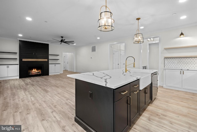 kitchen with hanging light fixtures, a kitchen island with sink, light stone counters, and light wood-type flooring