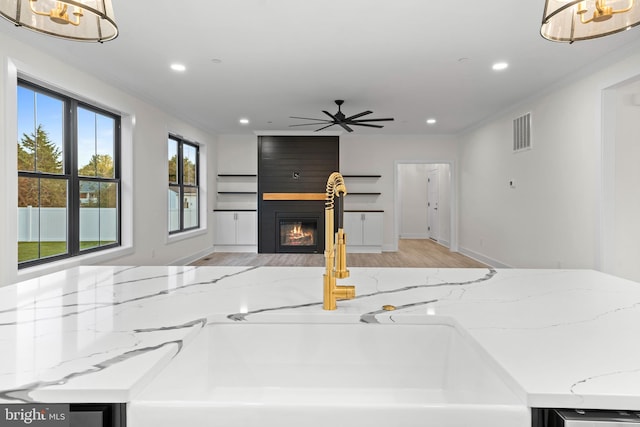 unfurnished living room featuring ornamental molding, ceiling fan with notable chandelier, a fireplace, and light hardwood / wood-style flooring