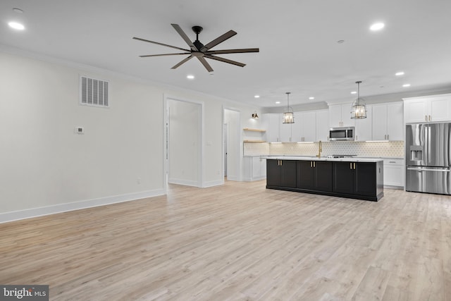 kitchen featuring pendant lighting, appliances with stainless steel finishes, a kitchen island with sink, backsplash, and white cabinets