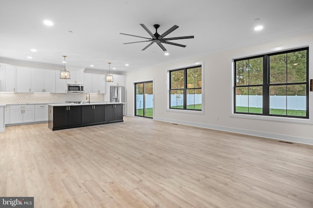 kitchen with a center island with sink, appliances with stainless steel finishes, pendant lighting, decorative backsplash, and white cabinets