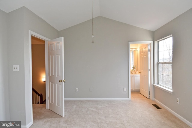 unfurnished bedroom with vaulted ceiling, light colored carpet, and ensuite bathroom