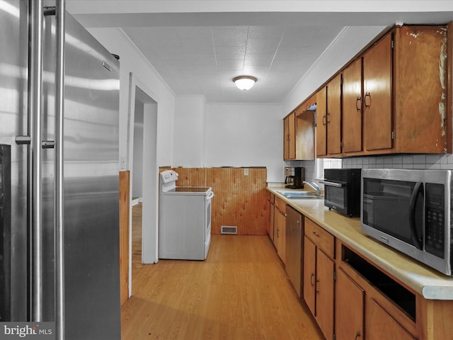 kitchen with appliances with stainless steel finishes, wooden walls, sink, crown molding, and light wood-type flooring