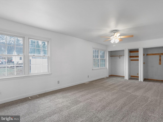 unfurnished bedroom featuring multiple closets, carpet floors, and ceiling fan